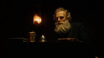 Movie still from “The Illusionist” (2006), directed by Neil Burger – An old man sitting at a table in front of a lit candle; Close Up shot, Low angle