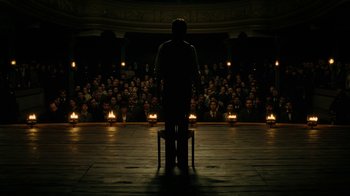 Movie still from “The Illusionist” (2006), directed by Neil Burger – A man standing in front of an audience in front of candles; Wide shot, Low angle