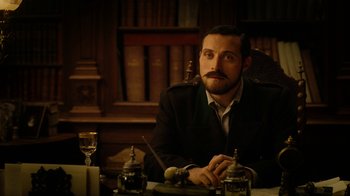 Movie still from “The Illusionist” (2006), directed by Neil Burger – A man sitting in front of a table with a glass of wine; Close Up shot, Low angle