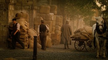 Movie still from “The Illusionist” (2006), directed by Neil Burger – Two men walking down a street near a pile of bags; Wide shot, High angle