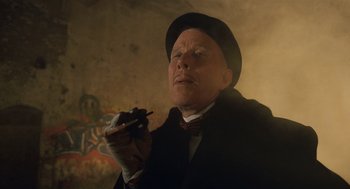 Movie still from “The Imaginarium of Doctor Parnassus” (2009), directed by Terry Gilliam – An older man in a black hat and a black coat holding a pen; Close Up shot, Low angle