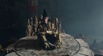 Movie still from “The Imaginarium of Doctor Parnassus” (2009), directed by Terry Gilliam – A man sitting on a stone platform holding a bowl of food; Wide shot, High angle
