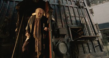 Movie still from “The Imaginarium of Doctor Parnassus” (2009), directed by Terry Gilliam – An old man with a long beard standing at the door of an old building; Wide shot, Low angle