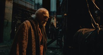 Movie still from “The Imaginarium of Doctor Parnassus” (2009), directed by Terry Gilliam – An old man with a long white beard standing next to a building; Medium shot, Over the shoulder angle