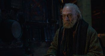 Movie still from “The Imaginarium of Doctor Parnassus” (2009), directed by Terry Gilliam – An old man with a long white beard sitting in a dark room; Medium shot, Over the shoulder angle