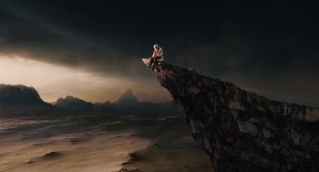Movie still from “The Imaginarium of Doctor Parnassus” (2009), directed by Terry Gilliam – A man sitting on top of a cliff on a surfboard; Extreme Wide shot, High angle