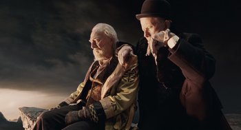 Movie still from “The Imaginarium of Doctor Parnassus” (2009), directed by Terry Gilliam – Two old men sitting next to each other on a cloudy day; Medium shot, Low angle