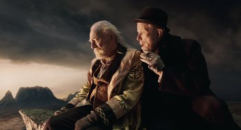 Movie still from “The Imaginarium of Doctor Parnassus” (2009), directed by Terry Gilliam – Two older men sitting next to each other on a hill; Medium shot, Low angle
