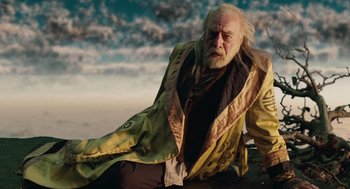Movie still from “The Imaginarium of Doctor Parnassus” (2009), directed by Terry Gilliam – An old man in a yellow coat sitting on the ground; Medium shot, Low angle