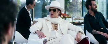 Movie still from “The Infiltrator” (2016), directed by Brad Furman – A man in a white suit and white hat sitting in a chair; Medium shot, Low angle