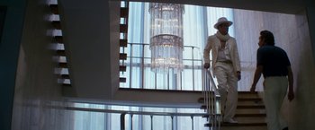 Movie still from “The Infiltrator” (2016), directed by Brad Furman – A man standing on top of a staircase next to a chandelier; Wide shot, Low angle