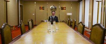 Movie still from “The Infiltrator” (2016), directed by Brad Furman – A man sitting at a long table in front of two empty wine glasses; Wide shot, Low angle