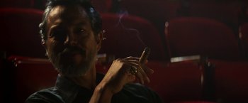 Movie still from “The Infiltrator” (2016), directed by Brad Furman – A man smoking a cigar while sitting in a chair; Close Up shot, Low angle