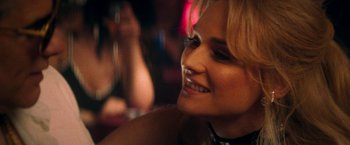 Movie still from “The Infiltrator” (2016), directed by Brad Furman – A woman smiling at a party; Close Up shot, Over the shoulder angle