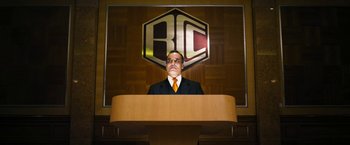 Movie still from “The Infiltrator” (2016), directed by Brad Furman – A man standing at a podium in front of a logo; Medium shot, Low angle