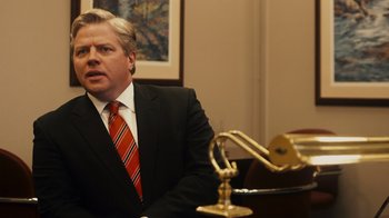 Movie still from “The Informant!” (2009), directed by Steven Soderbergh – A man wearing a suit and tie sitting at a desk; Close Up shot, Over the shoulder angle