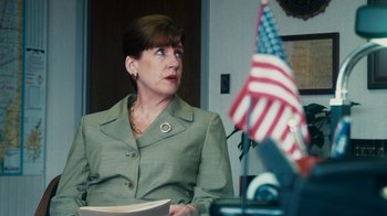 Movie still from “The Informant!” (2009), directed by Steven Soderbergh – A woman sitting in front of an american flag in an office; Close Up shot, Over the shoulder angle