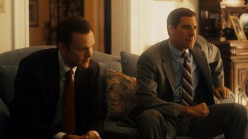 Movie still from “The Informant!” (2009), directed by Steven Soderbergh – A couple of men sitting on top of a couch next to each other; Medium shot, Over the shoulder angle