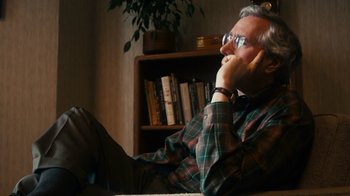 Movie still from “The Informant!” (2009), directed by Steven Soderbergh – An older man sitting in a chair with his hand on his face; Medium shot, Low angle