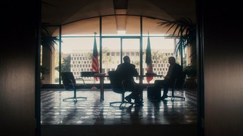 Movie still from “The Informant!” (2009), directed by Steven Soderbergh – Two men sitting at a table in front of a large window; Wide shot, Low angle