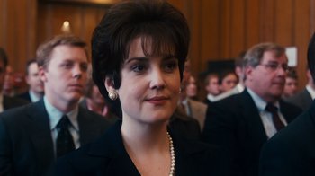 Movie still from “The Informant!” (2009), directed by Steven Soderbergh – A person wearing a suit and pearl necklace; Close Up shot, Over the shoulder angle