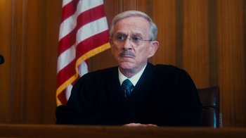 Movie still from “The Informant!” (2009), directed by Steven Soderbergh – An older man in a judge's robe in front of the american flag; Close Up shot, High angle