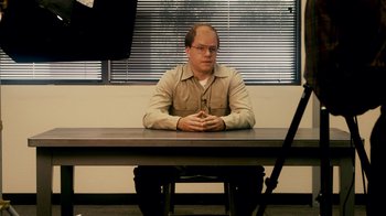 Movie still from “The Informant!” (2009), directed by Steven Soderbergh – A man sitting at a table in front of a camera; Medium shot, Over the shoulder angle