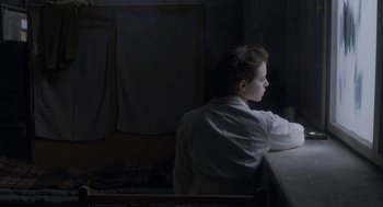 Movie still from “The Innocents” (2016), directed by Anne Fontaine – A person sitting at a table in a dark room; Medium shot, Over the shoulder angle