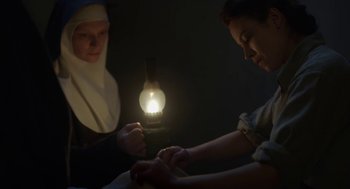 Movie still from “The Innocents” (2016), directed by Anne Fontaine – A nun lighting a candle in a dark room; Medium shot, High angle