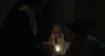 Movie still from “The Innocents” (2016), directed by Anne Fontaine – A group of people standing in a dark room; Medium shot, Low angle