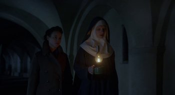 Movie still from “The Innocents” (2016), directed by Anne Fontaine – A nun holding a candle in front of a woman; Medium shot, Low angle