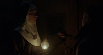 Movie still from “The Innocents” (2016), directed by Anne Fontaine – A nun is holding a light bulb in a dark room; Medium shot, Low angle