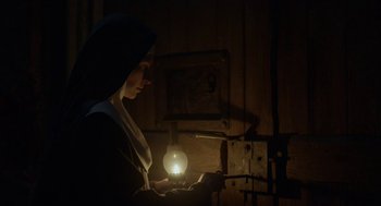 Movie still from “The Innocents” (2016), directed by Anne Fontaine – A woman holding a light in a dark room; Medium shot, Low angle