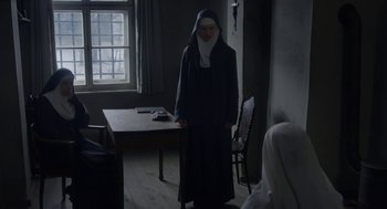 Movie still from “The Innocents” (2016), directed by Anne Fontaine – A woman dressed as a nun standing in front of a table; Wide shot, High angle