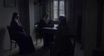 Movie still from “The Innocents” (2016), directed by Anne Fontaine – Two women sitting at a table in a room; Wide shot, High angle