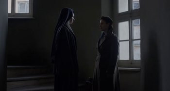 Movie still from “The Innocents” (2016), directed by Anne Fontaine – Two women are standing next to each other in front of a window; Medium shot, Low angle