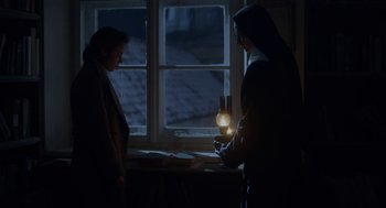 Movie still from “The Innocents” (2016), directed by Anne Fontaine – Two people standing in front of a window at night; Medium shot, Low angle