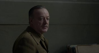 Movie still from “The Innocents” (2016), directed by Anne Fontaine – An older man in a military uniform looking to his left; Close Up shot, Over the shoulder angle