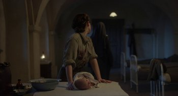 Movie still from “The Innocents” (2016), directed by Anne Fontaine – A woman standing next to a baby on a table; Medium shot, Low angle