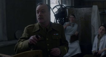 Movie still from “The Innocents” (2016), directed by Anne Fontaine – A man in a military uniform holding a doughnut; Medium shot, Over the shoulder angle