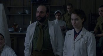 Movie still from “The Innocents” (2016), directed by Anne Fontaine – A group of people standing next to each other in a room; Medium shot, Over the shoulder angle