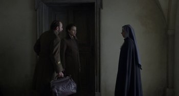 Movie still from “The Innocents” (2016), directed by Anne Fontaine – A man and a woman holding a bag and a woman wearing a nun's habit; Medium shot, Over the shoulder angle