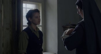 Movie still from “The Innocents” (2016), directed by Anne Fontaine – A man and a woman standing next to each other in front of a window; Medium shot, Over the shoulder angle