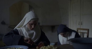 Movie still from “The Innocents” (2016), directed by Anne Fontaine – A nun is cutting potatoes with a knife; Medium shot, Low angle