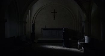 Movie still from “The Innocents” (2016), directed by Anne Fontaine – A person in a dark room next to a cross; Wide shot, Low angle