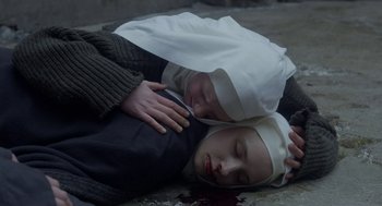 Movie still from “The Innocents” (2016), directed by Anne Fontaine – Two people in a hooded scarf laying on the ground; Close Up shot, Overhead angle
