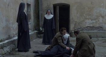Movie still from “The Innocents” (2016), directed by Anne Fontaine – A group of people standing next to each other on the ground; Wide shot, High angle