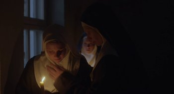 Movie still from “The Innocents” (2016), directed by Anne Fontaine – Two nuns are lighting a candle in the dark; Medium shot, Low angle