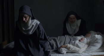 Movie still from “The Innocents” (2016), directed by Anne Fontaine – Two nuns are sitting on a bed and one nun is laying in bed; Medium shot, High angle