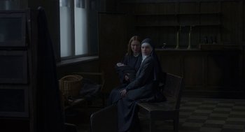 Movie still from “The Innocents” (2016), directed by Anne Fontaine – Two nuns sitting on a wooden bench in a room; Medium shot, Over the shoulder angle